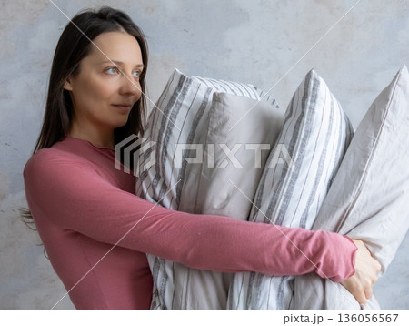 woman holds pile of pillows in her hands. pillows are in different colors, look like stack. woman holds pile of pillows in her hands. pillows are in different colors, look like stack. 136056567
