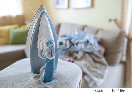 An iron on an ironing board with wrinkled linen in the background An iron on an ironing board with wrinkled linen in the background 136056660