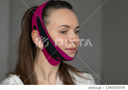 young woman in lifting bandage face mask for face contour correction and wrinkle control. Home facial skin care young woman in lifting bandage face mask for face contour correction and wrinkle control. Home facial skin care 136056704