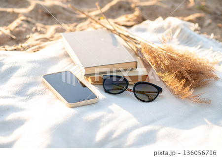 Minimal beach arrangement with tech and nature elements on a white blanket under warm sunshine Minimal beach arrangement with tech and nature elements on a white blanket under warm sunshine 136056716