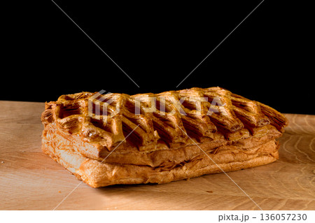 Confectionery, mesh-shaped puff pastry bun on wood board on black background Confectionery, mesh-shaped puff pastry bun on wood board on black background 136057230