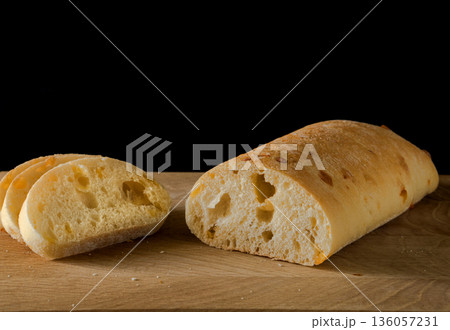 Ciabatta - Italian bread with cheese cut into slices on a wooden board on a black background Ciabatta - Italian bread with cheese cut into slices on a wooden board on a black background 136057231