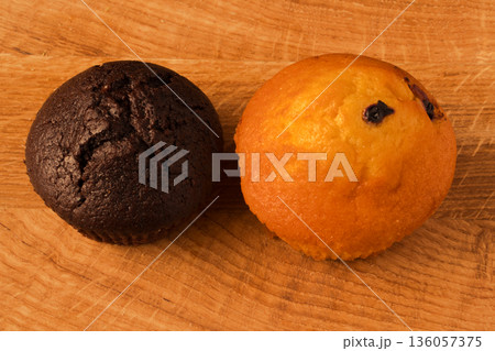 two cupcakes, one coffee-colored second light brown on a wooden board two cupcakes, one coffee-colored second light brown on a wooden board 136057375