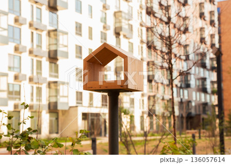 Wooden stylized bird feeder in form of small house against backdrop of modern apartment buildings, symbolizing care for birds and community living. Affordable housing, mortgages Wooden stylized bird feeder in form of small house against backdrop of modern apartment buildings, symbolizing care for birds and community living. Affordable housing, mortgages 136057614
