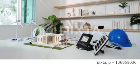 A model of a house is on a table with a blue hard hat and a solar panel 136058036