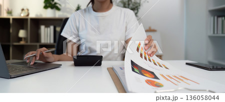 Business Analysis. Young woman reviewing financial documents and using a calculator. Business Analysis. Young woman reviewing financial documents and using a calculator. 136058044