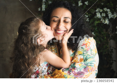 A lifestyle portrait of a white Caucasian mother and daughter embracing as the small girl gives her mom an affectionate kiss on the cheek 136058541