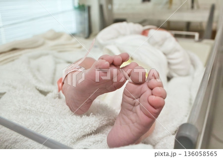 Closeup shot of tiny pair of feet and toes of newborn baby wrapped in a blanket wearing a plastic identity tag bracelet in the delivery room in hospital - concept of new life and motherhood Closeup shot of tiny pair of feet and toes of newborn baby wrapped in a blanket wearing a plastic identity tag bracelet in the delivery room in hospital - concept of new life and motherhood 136058565