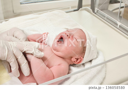 A newborn baby wearing a plastic identity bracelet being placed in a cot by a nurse in the delivery room at a maternity ward in hospital - concept of new life and motherhood 136058580