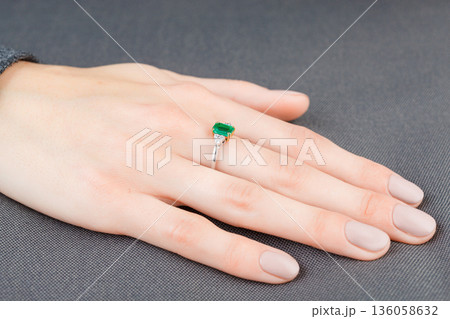 Beautiful female hand with gold ring with diamonds and emerald on gray background Beautiful female hand with gold ring with diamonds and emerald on gray background 136058632