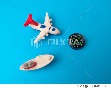 Small toy airplane, a toy boat, and a miniature compass on a blue background. Small toy airplane, a toy boat, and a miniature compass on a blue background. 136059070
