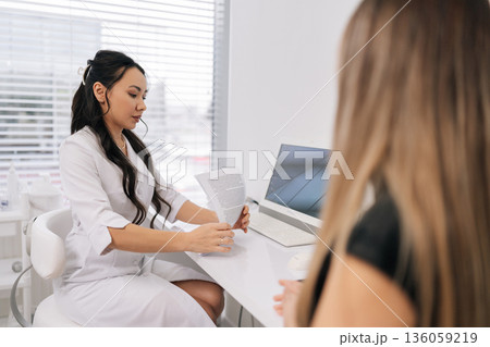 Female doctor holding woman patient documents, reviewing medical record data during healthcare consultation in clinic, discussing treatment plan and diagnosis for appointment. Female doctor holding woman patient documents, reviewing medical record data during healthcare consultation in clinic, discussing treatment plan and diagnosis for appointment. 136059219