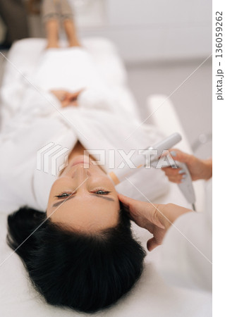 Close-up headshot of adult woman receiving non-invasive facial lifting ultrasound treatment in modern cosmetology clinic, focusing on anti-aging and skin rejuvenation for beauty and wellness. Close-up headshot of adult woman receiving non-invasive facial lifting ultrasound treatment in modern cosmetology clinic, focusing on anti-aging and skin rejuvenation for beauty and wellness. 136059262