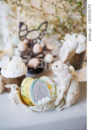 Easter cookies and rabbit figurines on spring table with cakes and eggs, soft light 136059278