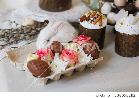 White bunny with chocolate eggs and roses in carton, Easter still life, soft bokeh 136059292