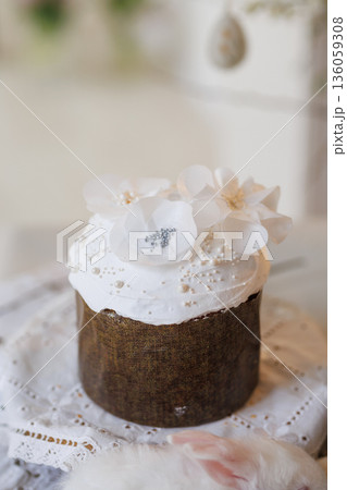 Easter cake with white icing and flower topper on lace cloth, soft minimal background 136059308