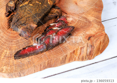 Cured beef meat sits on wooden board with some slices placed beside it food preparation. 136059313