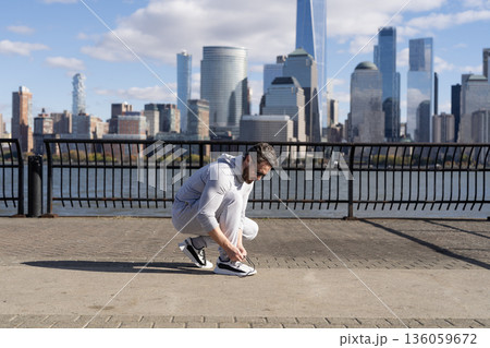 Fitness man tying lace of sports shoes. Athlete getting ready for workout wearing shoes sitting on floor. Sportsman tying sneakers. Athletic shoes. Fitness man tie shoelaces outdoor. Shoe lace 136059672