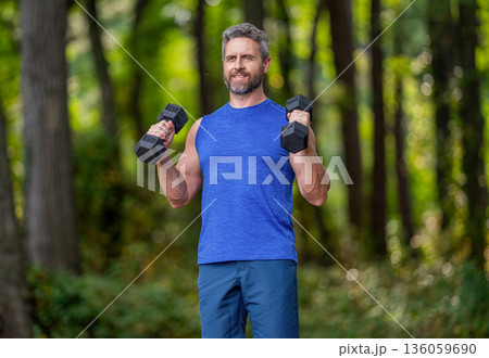 Strong triceps. Man exercising with dumbbell. Man athlete lifting dumbbell. Strong man do sport workout. Outdoor workout. Sport athlete man with dumbbell. Healthy lifestyle. Biceps muscle Strong triceps. Man exercising with dumbbell. Man athlete lifting dumbbell. Strong man do sport workout. Outdoor workout. Sport athlete man with dumbbell. Healthy lifestyle. Biceps muscle 136059690