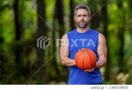 Man has sport motivation. Sport and hobby. Sportsman dunk in basket. Sport banner with copy space. Summer activity. Man with basketball ball in forest. Professional basketball player training outdoor 136059691