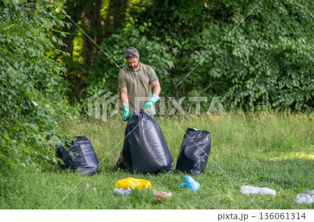 Garbage collecting in forest. Ecology concept. Volunteer collecting garbage. Man in rubber gloves with trash bag clean up garbage. Man collecting plastic trash. Eco volunteer. Plastic waste problem Garbage collecting in forest. Ecology concept. Volunteer collecting garbage. Man in rubber gloves with trash bag clean up garbage. Man collecting plastic trash. Eco volunteer. Plastic waste problem 136061314