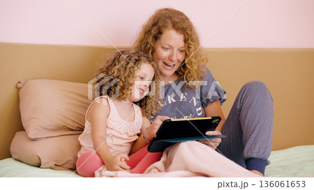 Mother and daughter having fun with digital tablet in bed Mother and daughter having fun with digital tablet in bed 136061653