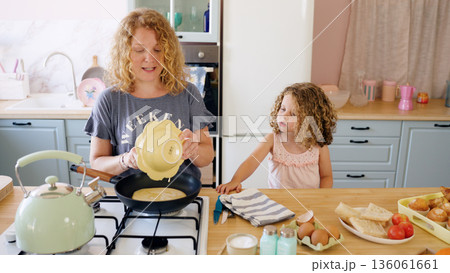 Mother and daughter cooking pancakes in kitchen 136061661