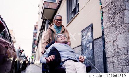 Woman assisting man using wheelchair on city street Woman assisting man using wheelchair on city street 136061719