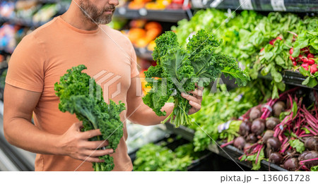 Man shopping kale cabbage in grocery store. Healthy lifestyle. Fresh food store. Man in grocery store. Man shopping in vegetable supermarket. Grocery consumer with kale cabbage. Raw kale cabbage Man shopping kale cabbage in grocery store. Healthy lifestyle. Fresh food store. Man in grocery store. Man shopping in vegetable supermarket. Grocery consumer with kale cabbage. Raw kale cabbage 136061728