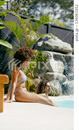 Women relaxing by tropical swimming pool with waterfall 136061852