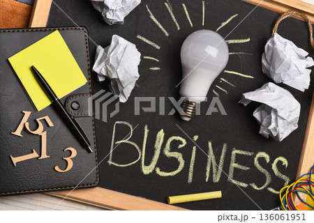 Chalkboard with wrinkled paper, notepad, pen, numerals and lamp. 136061951