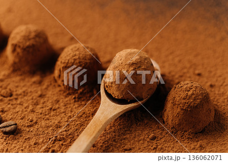 Cocoa truffles on wooden spoon in cocoa powder, closeup 136062071
