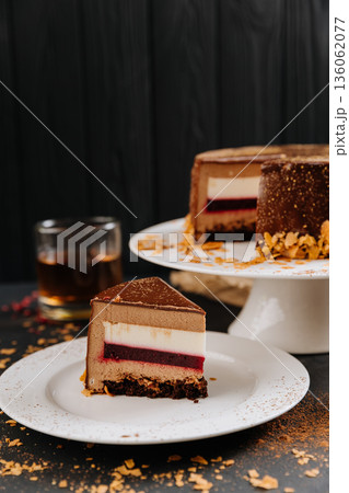 Chocolate mousse cake slice with berry layer on plate, cocoa dust, dark backdrop 136062077