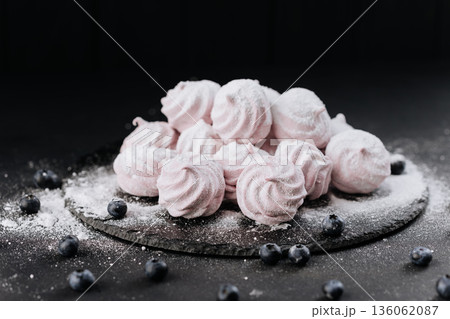 Pink meringue cookies with blueberries and falling sugar on slate, dark background Pink meringue cookies with blueberries and falling sugar on slate, dark background 136062087