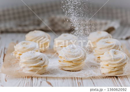 Powdered sugar falling on vanilla zephyr rosettes on parchment, rustic background Powdered sugar falling on vanilla zephyr rosettes on parchment, rustic background 136062092