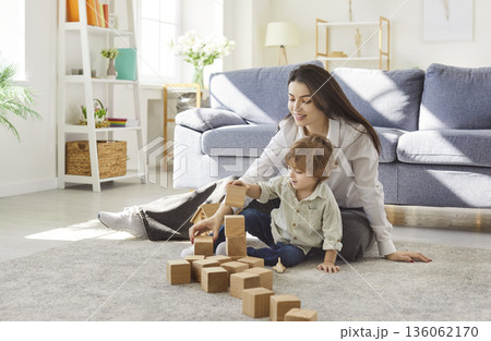 Mother and child building wooden blocks together on carpet in bright living room 136062170