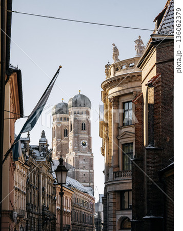 Historic Munich Old Town Street With Cathedral Of Our Dear Lady: Narrow Urban Alley Framing Iconic Twin Domed Church Towers And Traditional Bavarian Architecture Historic Munich Old Town Street With Cathedral Of Our Dear Lady: Narrow Urban Alley Framing Iconic Twin Domed Church Towers And Traditional Bavarian Architecture 136062379
