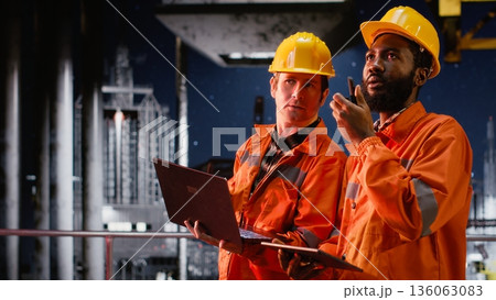 Environmental officers on marine oil platform communicate via radio to assess extraction data, control and maintain balance of natural fuel and petroleum from the ocean ecosystem. 136063083