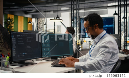 Programmer in office using AI LLM chatbot to get help optimizing systems performance metrics. IT worker in tech agency utilizing generative AI LLM assistant for faster software development, camera A 136063151