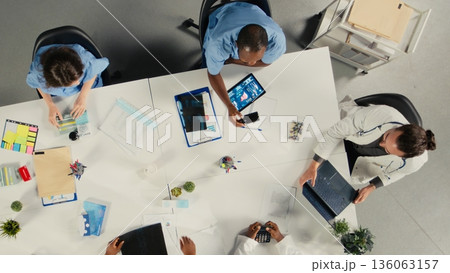Top down view of surgeons staff in a clinic discussing therapy options and research analysis. The meeting highlights professionalism and innovation in healthcare planning. 136063157