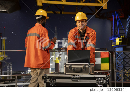 Offshore engineer monitoring oil extraction on offshore platform, using laptop to assess emission tracking for performance. Ensuring oil and gas drilling operations under northern lights. Offshore engineer monitoring oil extraction on offshore platform, using laptop to assess emission tracking for performance. Ensuring oil and gas drilling operations under northern lights. 136063344
