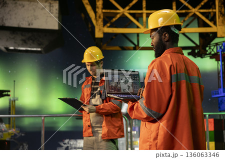Environmental officer uses laptop on offshore rig under the northern lights, ensuring petroleum and fuel extraction on the platform. Compliance with oil and gas production industry. Environmental officer uses laptop on offshore rig under the northern lights, ensuring petroleum and fuel extraction on the platform. Compliance with oil and gas production industry. 136063346