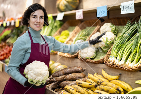 Woman shop seller puts cauliflower goods on display case Woman shop seller puts cauliflower goods on display case 136065399