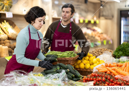 Woman seller puts cucumbers man seller puts green peas Woman seller puts cucumbers man seller puts green peas 136065441