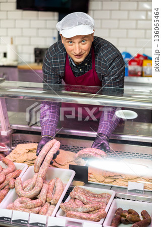 Butcher offering fresh raw sausages displayed in glass showcase 136065464
