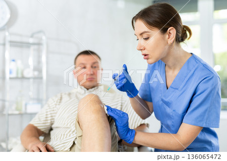 Female doctor performs intra-articular injection treatment of knee bursitis to man patient Female doctor performs intra-articular injection treatment of knee bursitis to man patient 136065472
