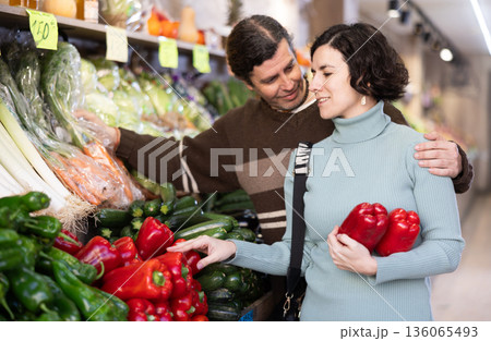 Married couple selects fresh bell peppers, tomatoes and other vegetables at supermarket counter Married couple selects fresh bell peppers, tomatoes and other vegetables at supermarket counter 136065493