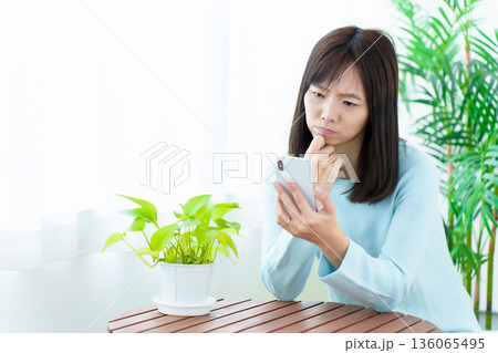 困った顔をしてスマートフォンを使う主婦 136065495