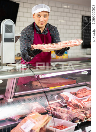 Adult man puts beef ribs in showcase 136065508