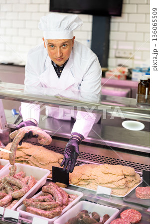 Adult man puts meat sausages in showcase Adult man puts meat sausages in showcase 136065509